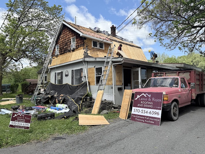 Lema and Rojas roofing crew working on a residential roof replacement with jobsite signs visible.